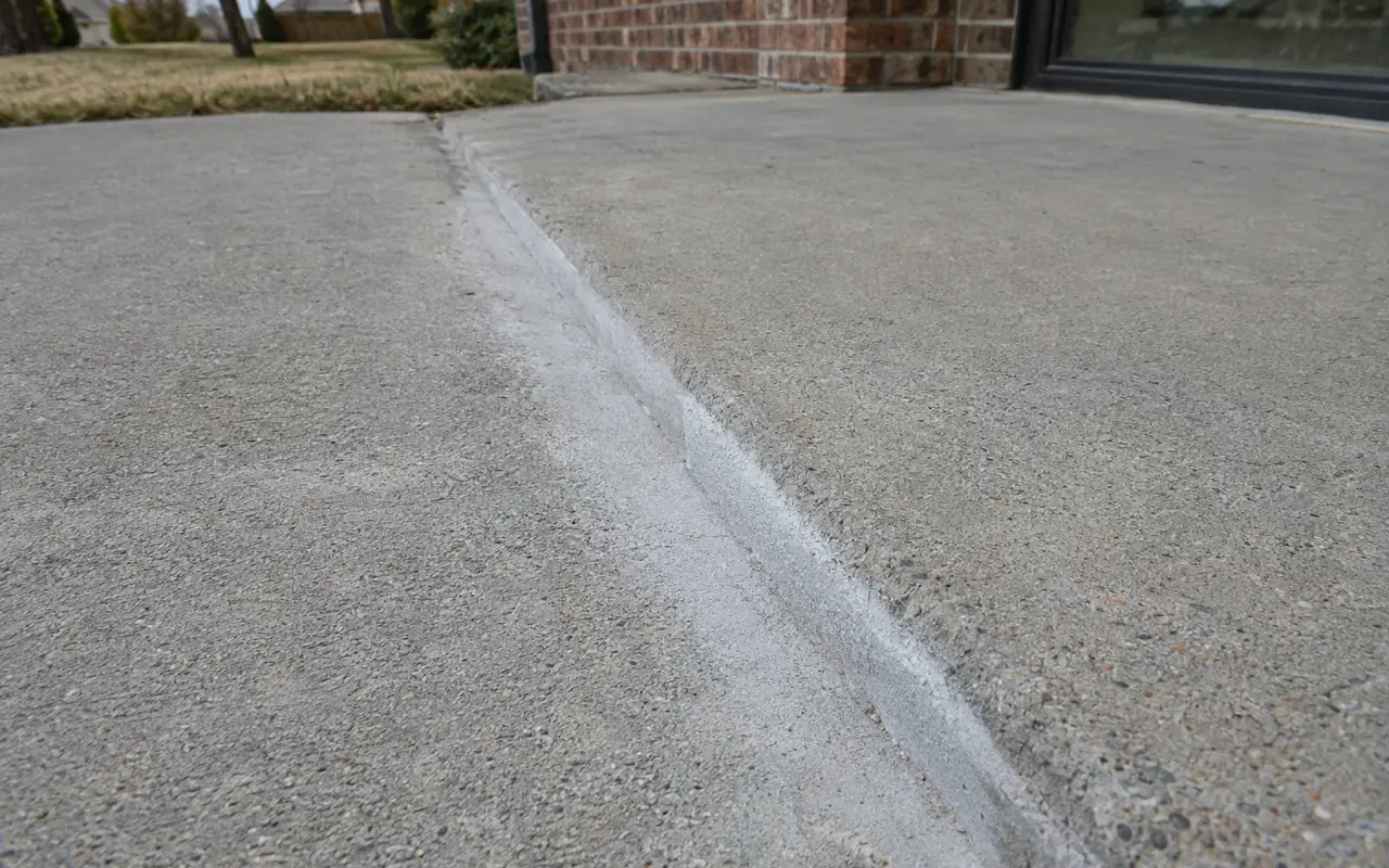 Close-up of a ground, beveled concrete sidewalk edge beside an untouched slab.